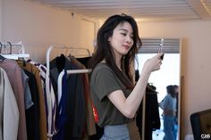 a woman is looking at her cell phone while standing in front of a rack of clothes