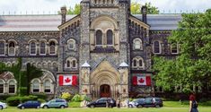 people are walking in front of an old building with canadian flags hanging from it's windows