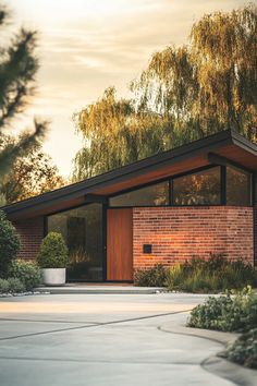 a brick house with trees in the back ground and bushes on either side of it