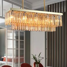 a chandelier hanging over a dining room table with red chairs and a potted plant