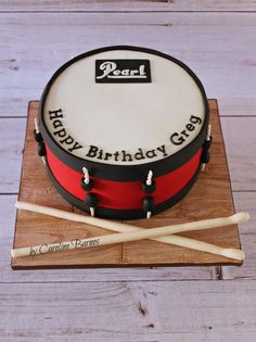 a birthday cake that is on top of a wooden board with two drums in front of it