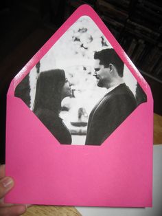 a person holding up a pink envelope with a photo inside