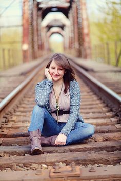 a young woman sitting on train tracks with her hand under her chin and looking at the camera