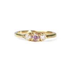 a yellow gold ring with three diamonds on the side and a pink sapphire in the middle