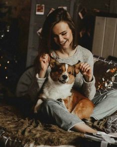 a woman combs her dog's hair while sitting on a bed in front of a christmas tree