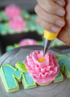 a person is decorating some cookies with icing and a flower on top that reads m