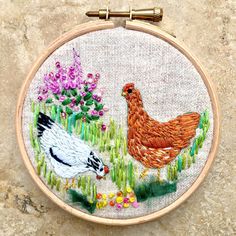 an embroidery project with two chickens and flowers in the grass, on a stone surface