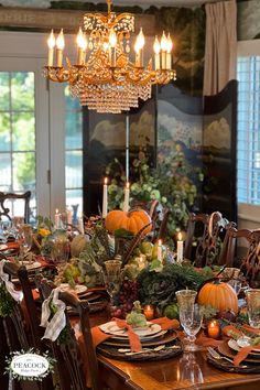 a dining room table is set with pumpkins, greenery and candles for the centerpiece