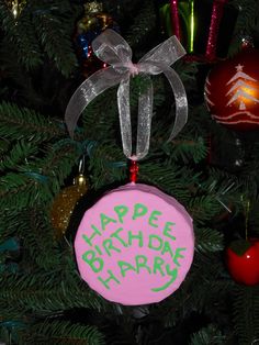 a pink ornament hanging from the side of a christmas tree with green writing on it