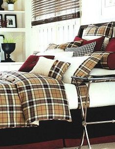 a bed with plaid comforter and pillows on it next to a white bookcase