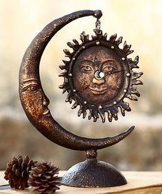 a metal sun and moon decoration sitting on top of a wooden table next to a pine cone