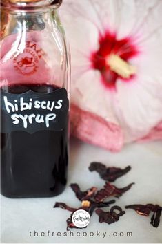 a bottle filled with black liquid next to a pink flower and some other items on the table