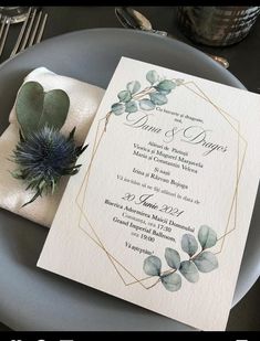 an elegant wedding card with greenery on the front and back, sitting on top of a plate