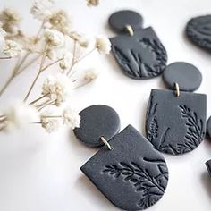 some black earrings are laying on a white surface next to flowers and dried grass in the background