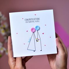 someone holding up a congratulations card with two buttons on the front and one button on the back