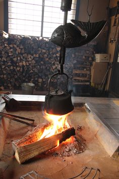 an iron pot is cooking over a fire in a room with wood and logs on the floor