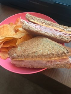 a pink plate topped with a sandwich and chips