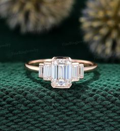 an emerald cut diamond ring sitting on top of a green blanket