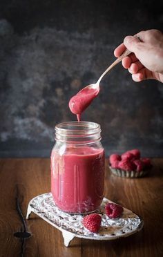 a person is dipping raspberry sauce into a jar