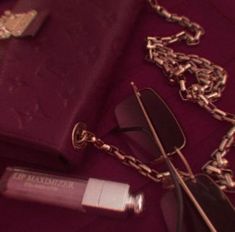 a pair of sunglasses, lipstick and chain on a purple surface