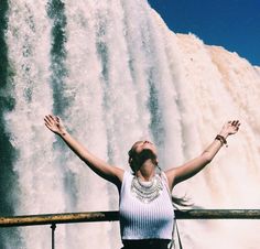 a woman standing in front of a waterfall with her hands up and arms wide open