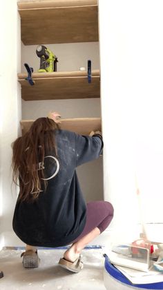 a woman kneeling on the floor in front of shelves