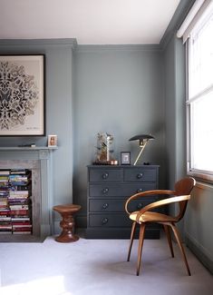 a living room with a chair, dresser and fire place in front of a window