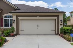 a house with two garages in front of it and landscaping around the driveway area