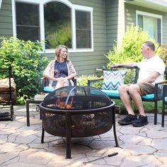 two people sitting around a fire pit on a patio with chairs and table in the background