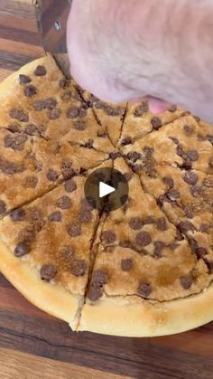 someone cutting into a chocolate chip pizza on top of a wooden table