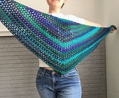 a woman is holding up a crocheted shawl