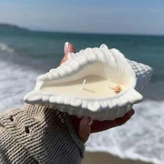 a person holding up a seashell with a candle in it near the water's edge