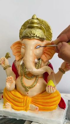 a person is painting the face of an elephant figurine with gold paint on it's body