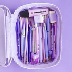 a white case filled with lots of different types of pens and pencils on top of a purple surface