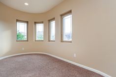 an empty room with three windows and carpeted flooring in front of the window