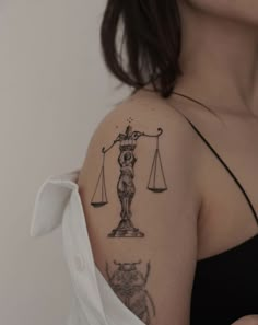 a woman with a tattoo on her shoulder holding a scale of justice and a cat