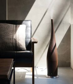 a large vase sitting next to a black chair in a room with sunlight coming through the window