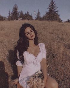 a woman sitting in the grass with her eyes closed and holding a bouquet of flowers