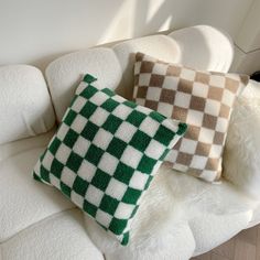 two green and white checkered pillows sitting on top of a white couch next to each other