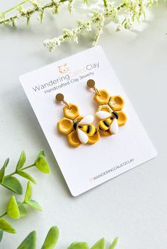 a pair of yellow and white earrings sitting on top of a card next to flowers