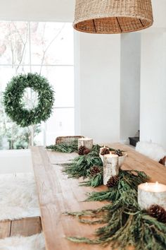 a wooden table topped with pine cones and greenery next to a wreath hanging from the ceiling