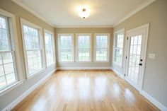 an empty room with wood floors and three windows on the far wall is a door leading to another room