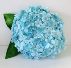 a close up of a blue flower on a white surface with green leafy stems