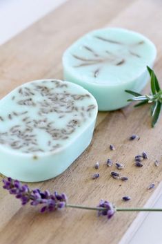 two soap bars sitting on top of a wooden cutting board next to lavender and rosemary