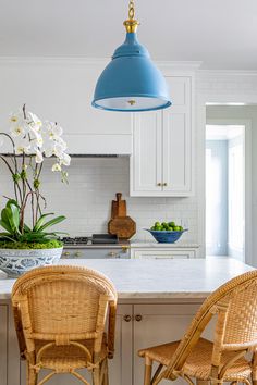 two wicker chairs sit in front of an island with white countertops and blue pendant lights