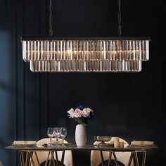 a chandelier hanging over a dining room table with white chairs and plates on it