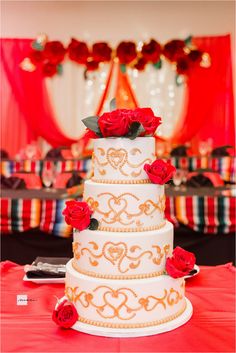 a three tiered wedding cake with red roses on the top and bottom, sitting on a table