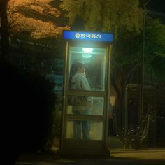 a man standing in a phone booth on the side of a road at night time