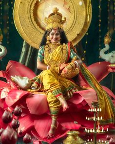 a woman sitting on top of a red flower next to a gold plate and candles