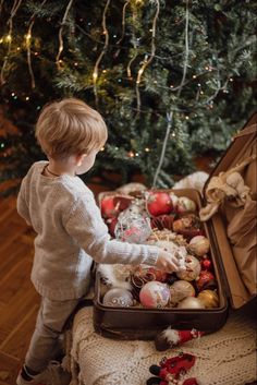 a little boy that is standing in front of a christmas tree with ornaments on it